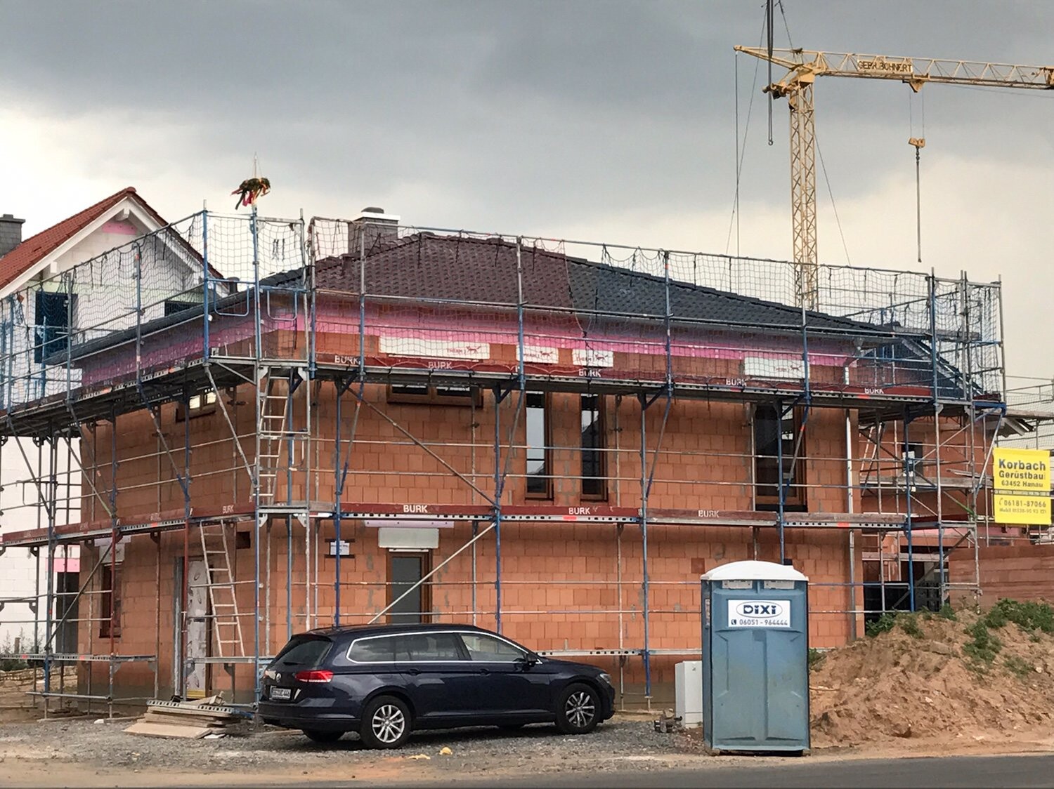 Zweistöckiger Rohbau mit Gerüst, Baukran, Bau-WC und Fahrzeug auf Baustelle