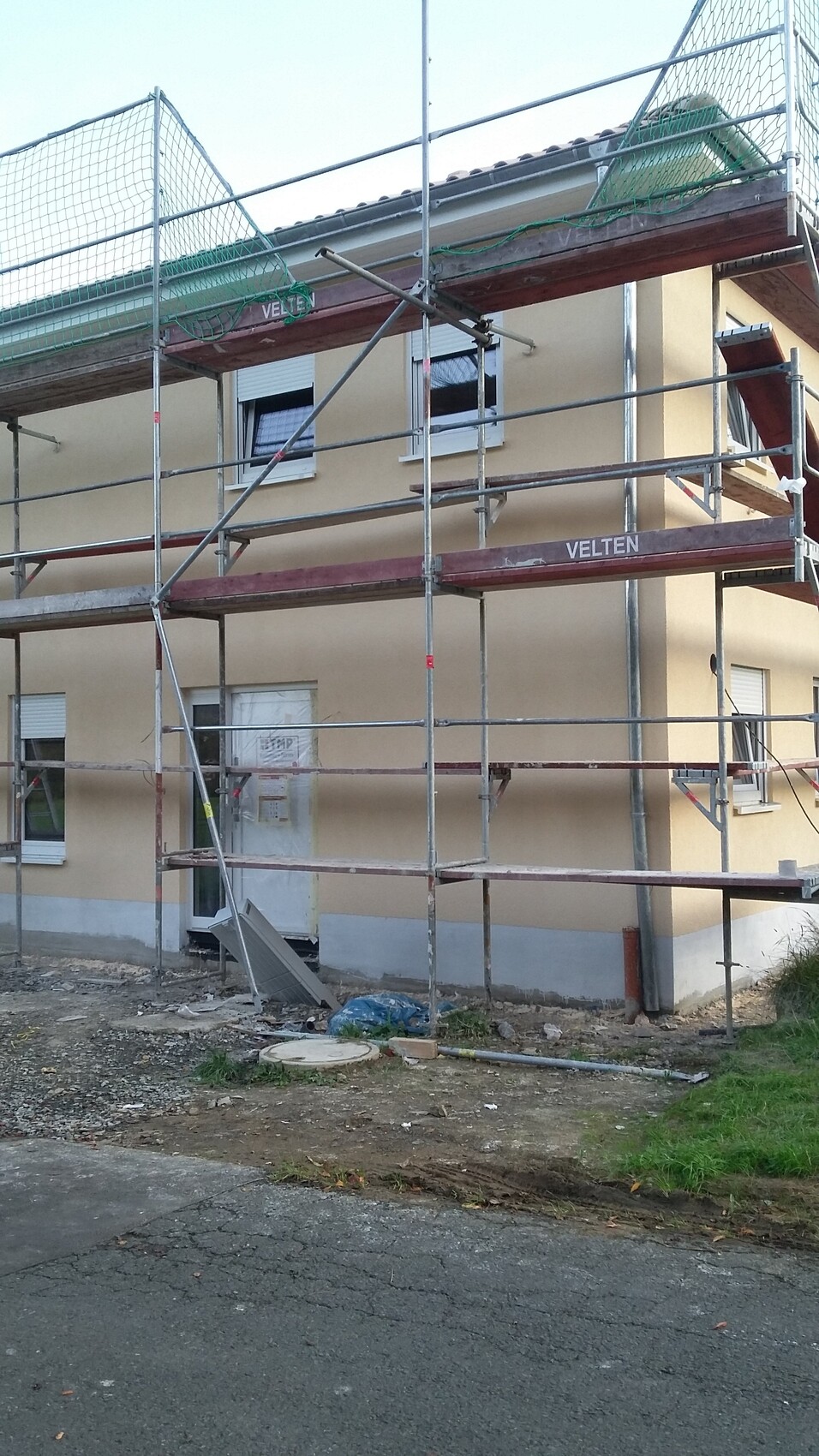 Gerüstbau an gelbem Wohngebäude; Baugerüst, Bodenchaos, Eingangstür sichtbar