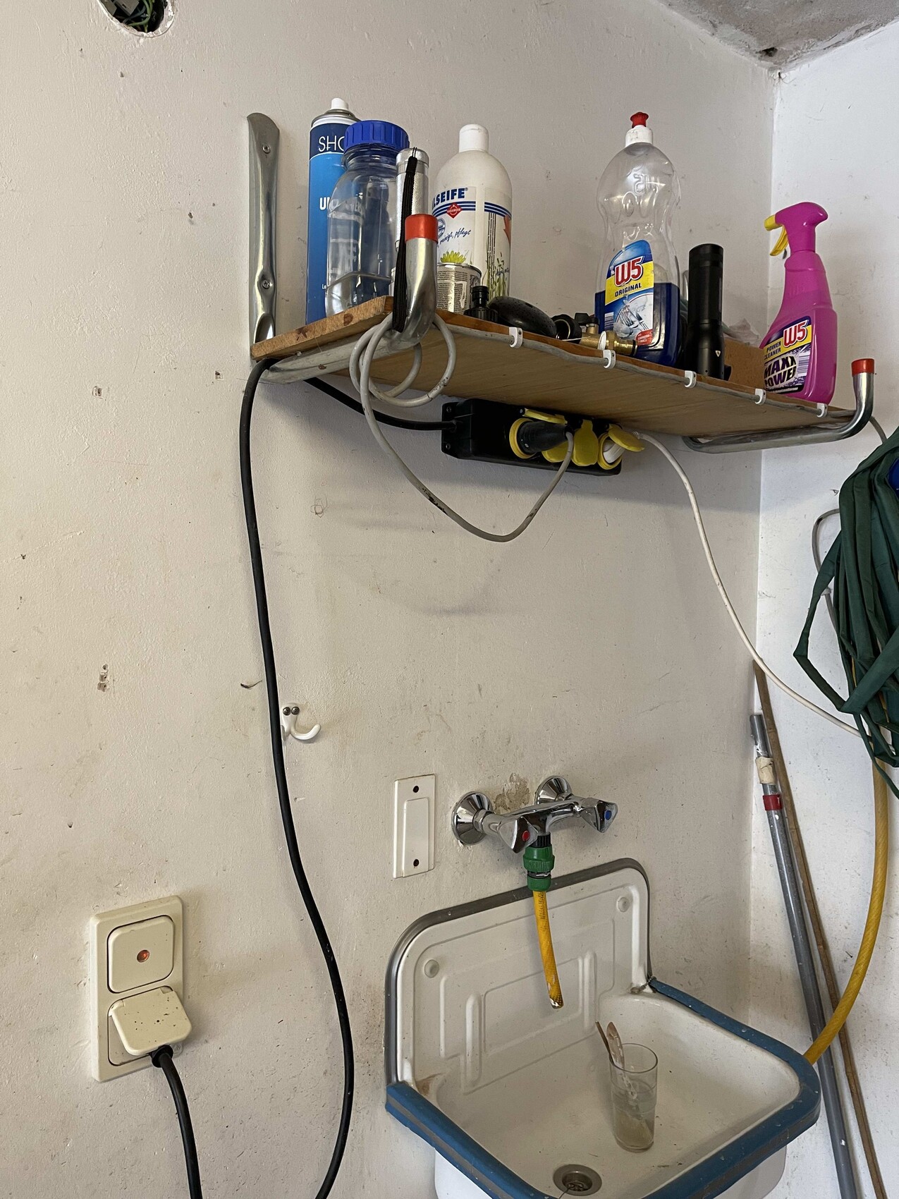 Waschküche mit Regal voller Reinigungsmittel über dem Waschbecken; Schlauch liegt unten.