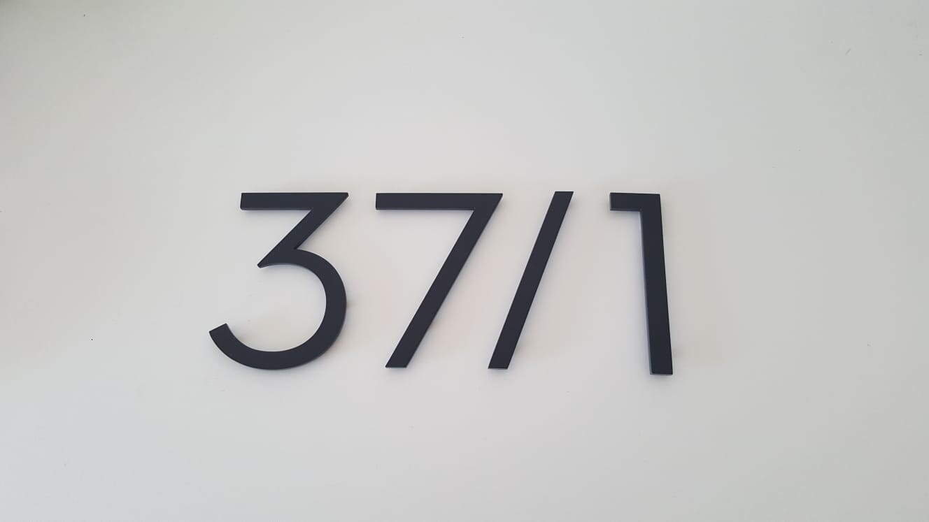 Schwarze Ziffern 3771 als Wand-Dekoration auf weißem Hintergrund.