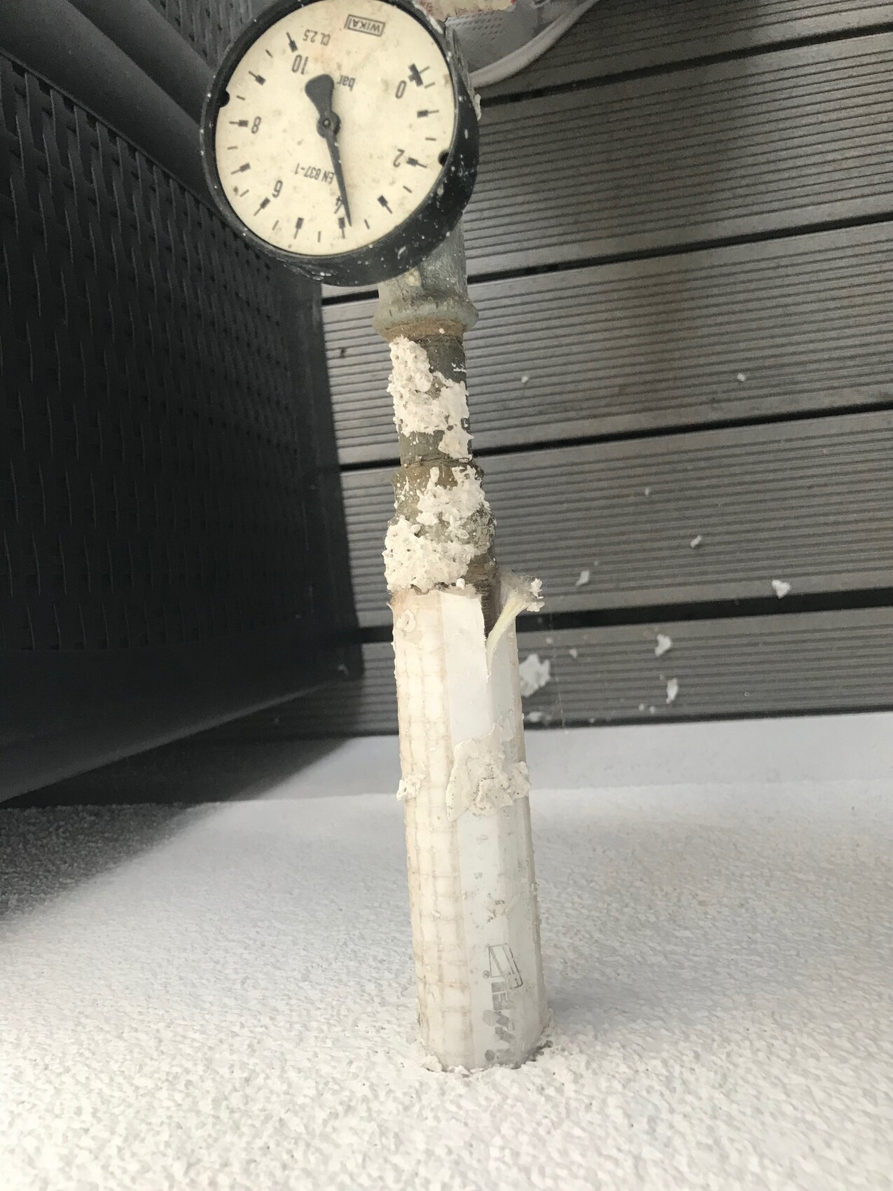 Druckmessgerät an Rohr mit abplatzender Isolierung vor verschneitem Hintergrund