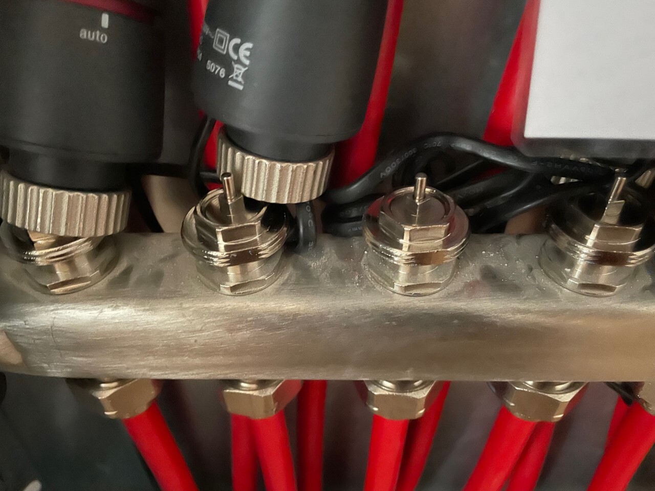 Nahaufnahme einer Klemmenleiste mit roten Kabeln und Metallmuttern auf einer Metallstange.