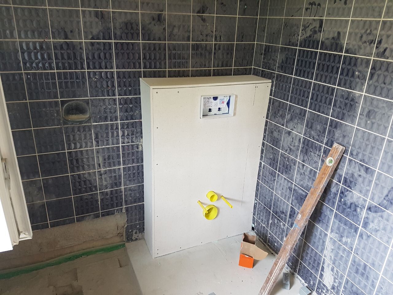 Weißer Elektrik-Verteiler mit Zähler an dunkler Fliesenwand; gelbe Abdeckkappen am Schrank.