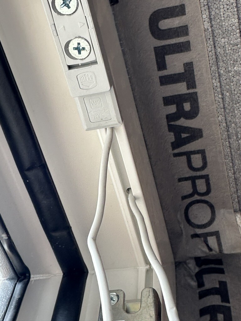 Nahaufnahme elektrischer Anschlusspunkte mit Klemmen und weißen Kabeln am Türrahmen