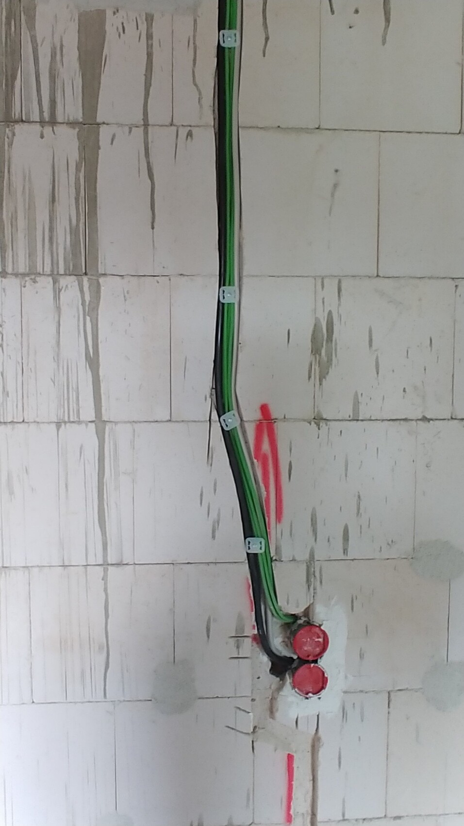 Verlegte grüne und schwarze Kabel an einer weiß verputzten Wand, rote Endkappen sichtbar.