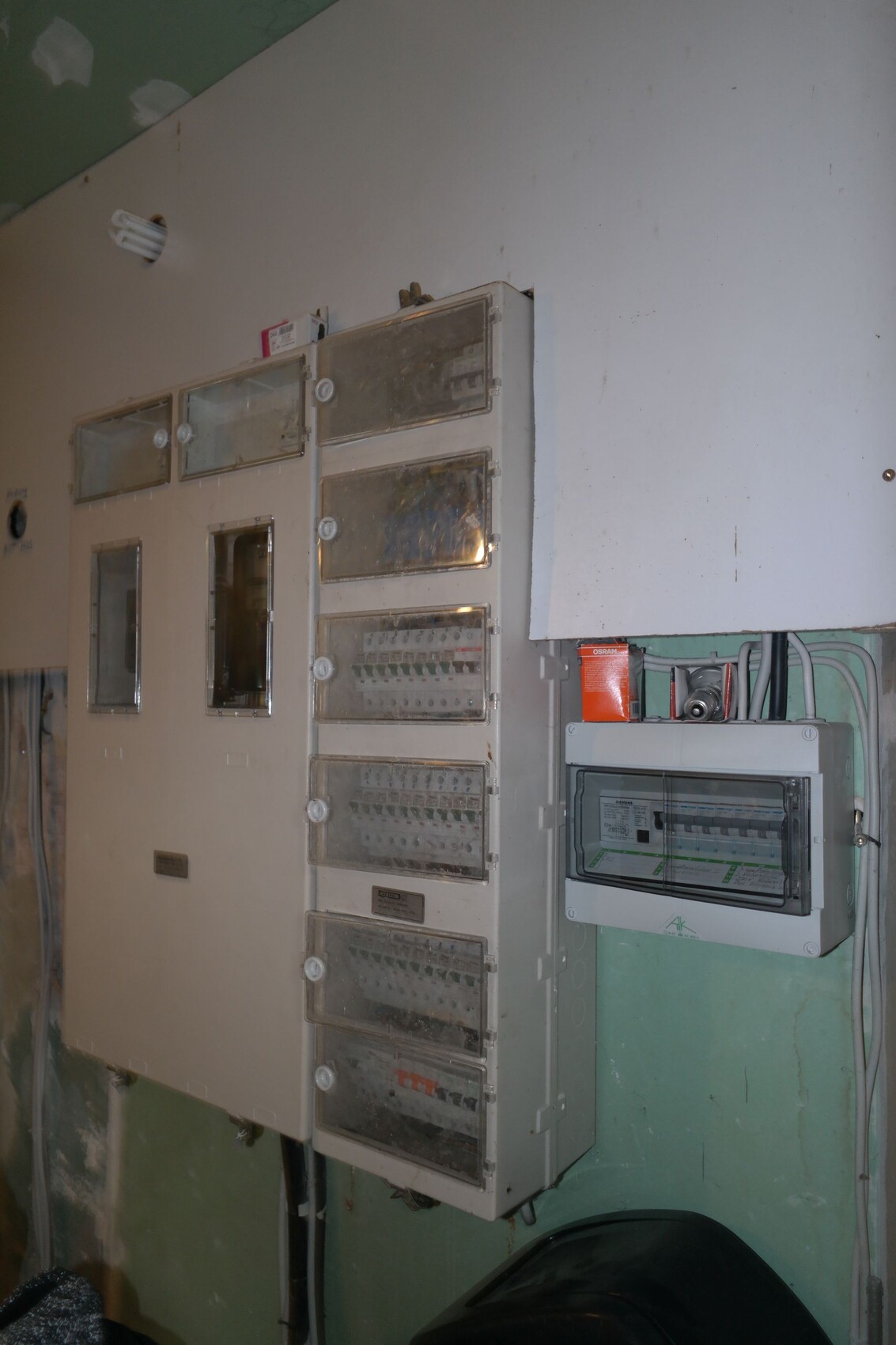 Sicherungskästen mit Glasdeckeln und Zähler an einer Wand im Keller.