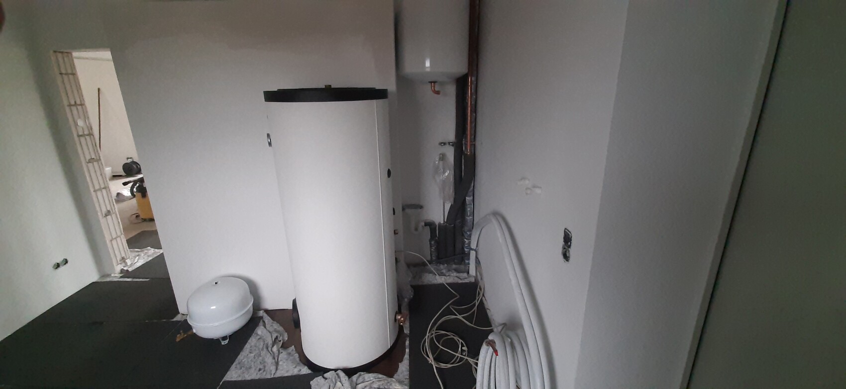 Keller-Heizungsraum: großer weißer Warmwasserspeicher, Ausdehnungsgefäß, Rohre.