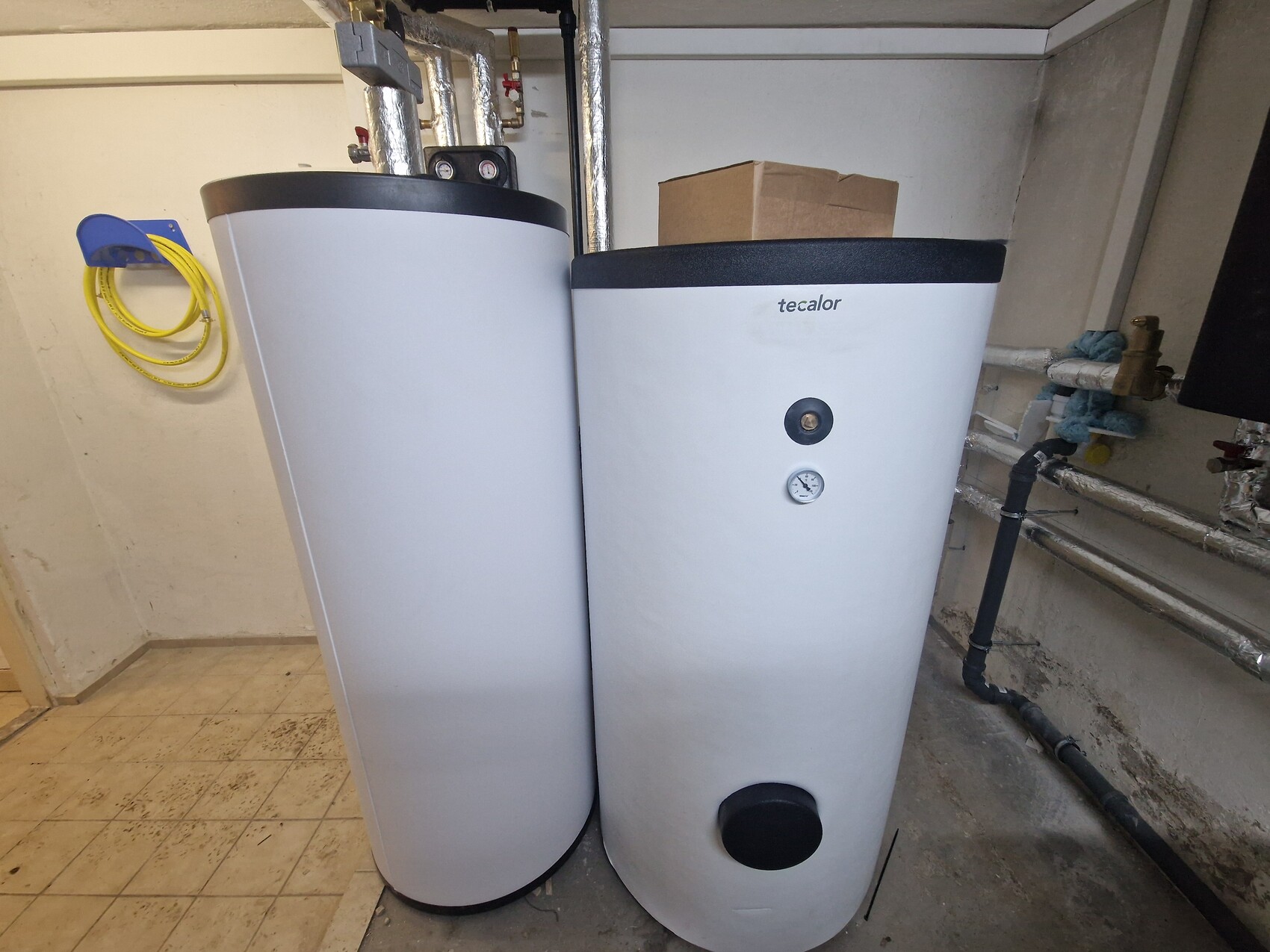 Zwei weiße Warmwasserspeicher im Keller mit Rohren und Druckanzeige