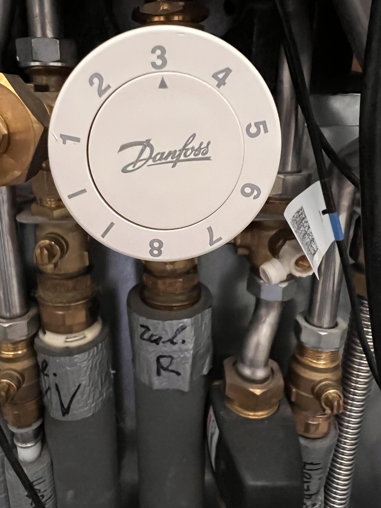 Nahaufnahme eines Danfoss Heizungsventils mit Skala 1–9 und Rohrleitungen dahinter.