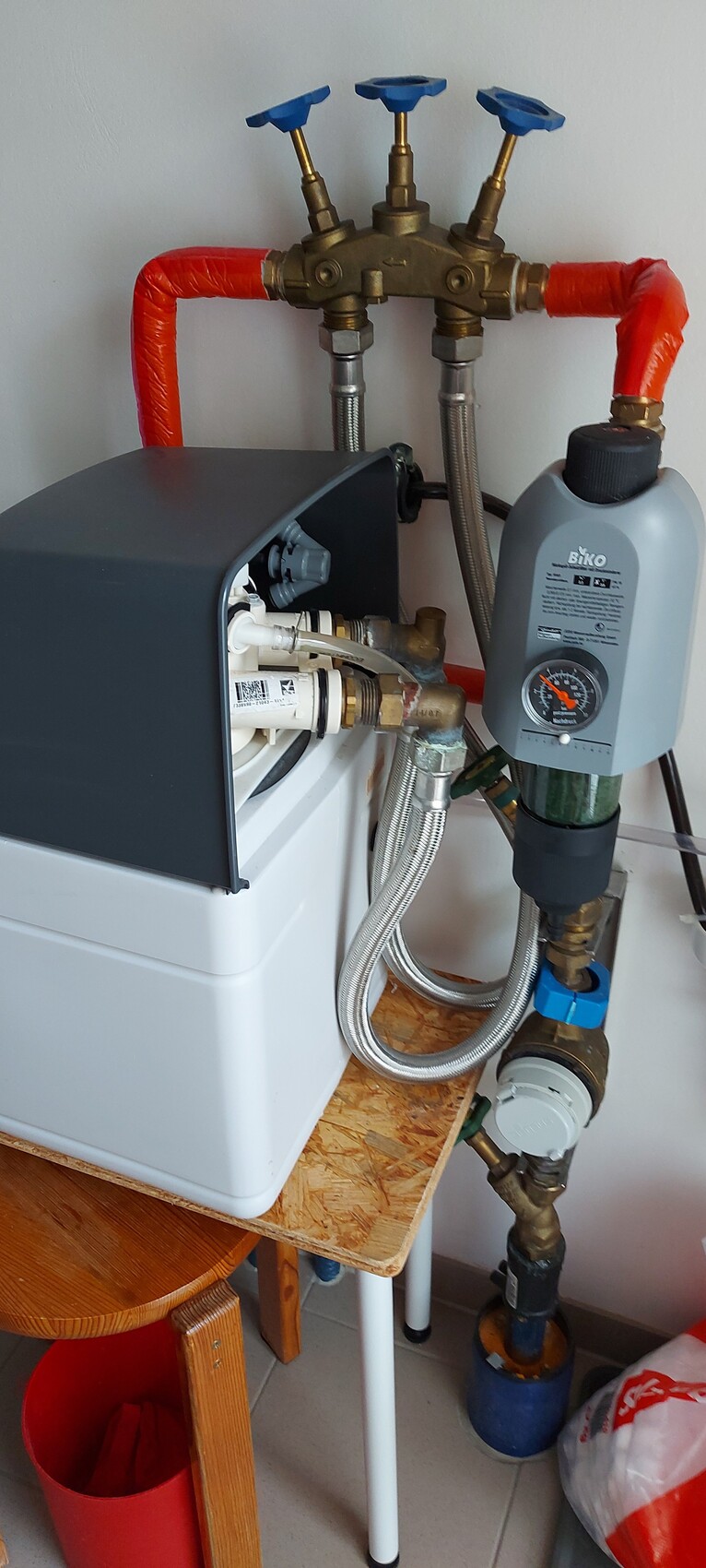 Heizungs- und Sanitäranlage mit drei blauen Ventilen, rotem isolierten Rohr und Messgerät.