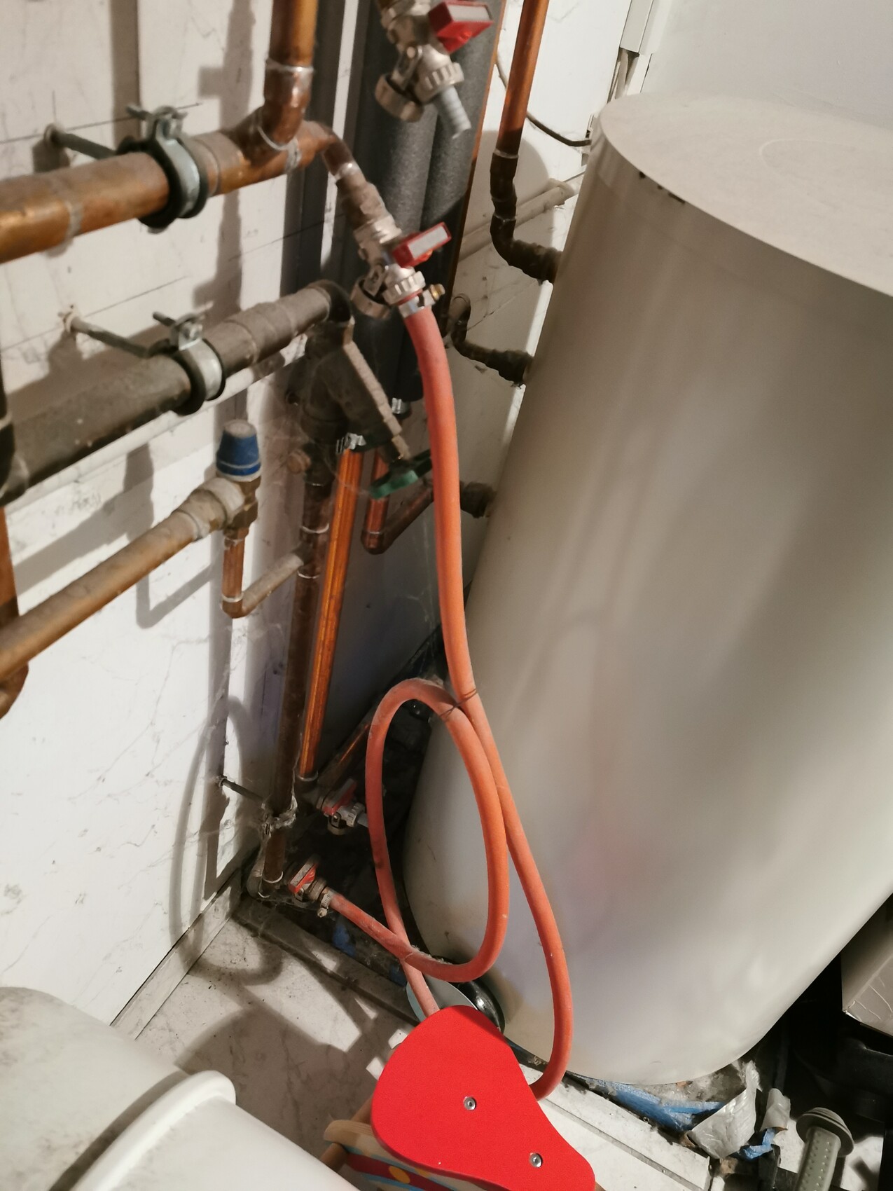 Warmwasserspeicher mit Kupferleitungen, roten Absperrventilen und rotem Schlauch im Heizraum.