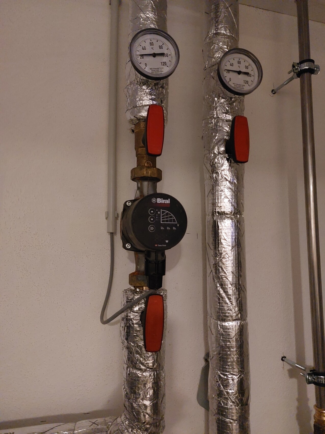 Zwei Druckmesser an isolierten Heizungsrohren mit roten Absperrventilen