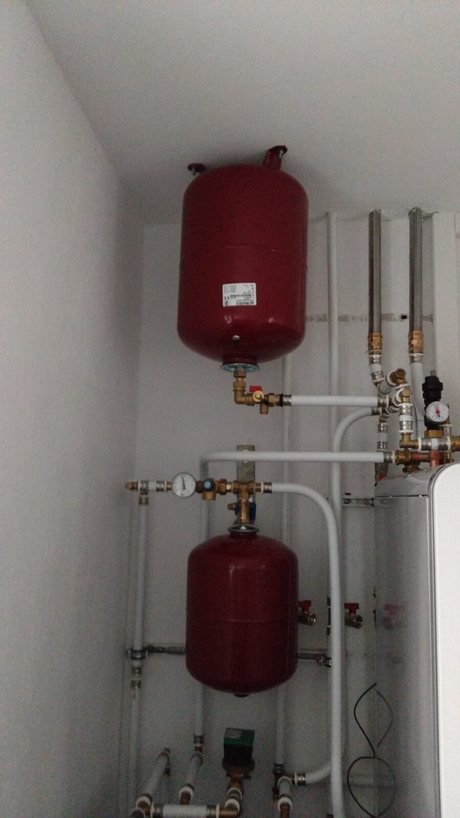 Zwei rote Ausdehnungsbehälter in Heizungsanlage, Rohrleitungen, Ventile und Druckmessgerät.
