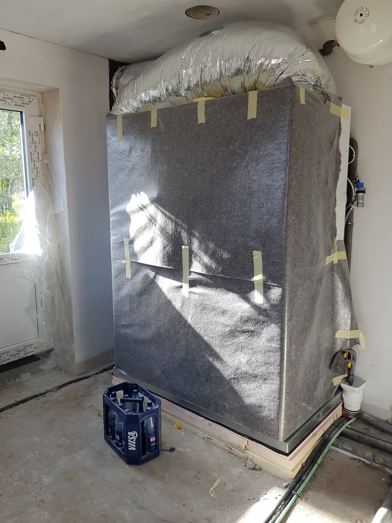 Großes, isoliertes Heiz-/Kühlgerät in silberner Folie mit Rohren in einem Bauzimmer.