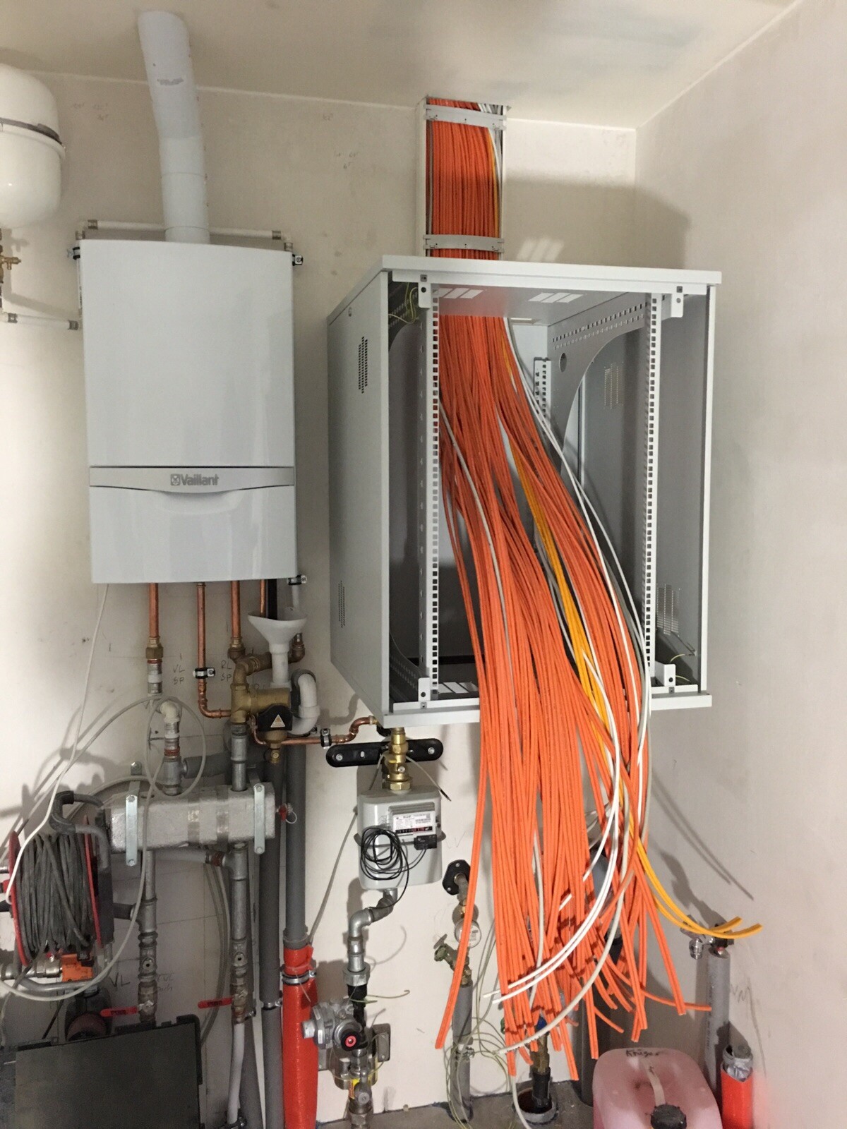 Heizungsraum mit Vaillant-Boiler und offenem Schaltschrank mit vielen orange Kabeln.