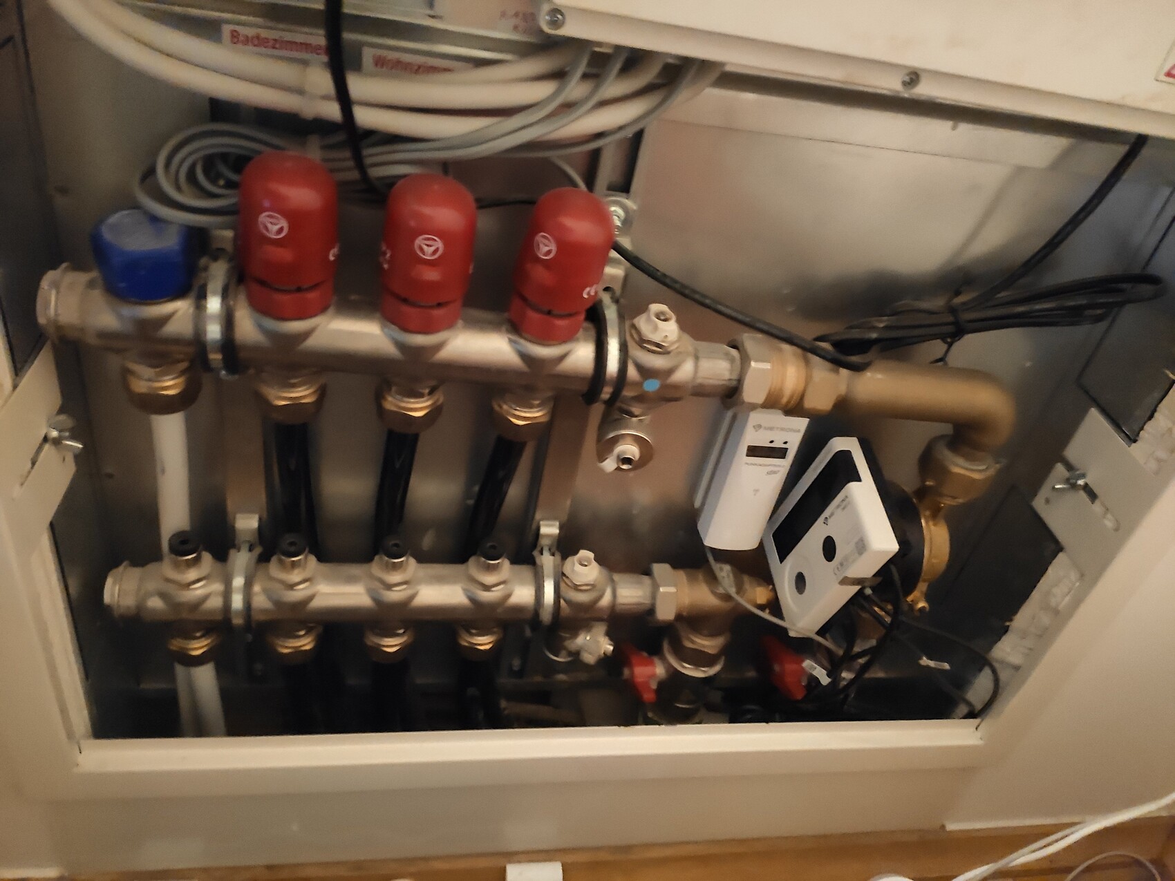 Heizungsverteilersystem mit roten Absperrventilen, Kupferrohren und elektrischer Steuerung.