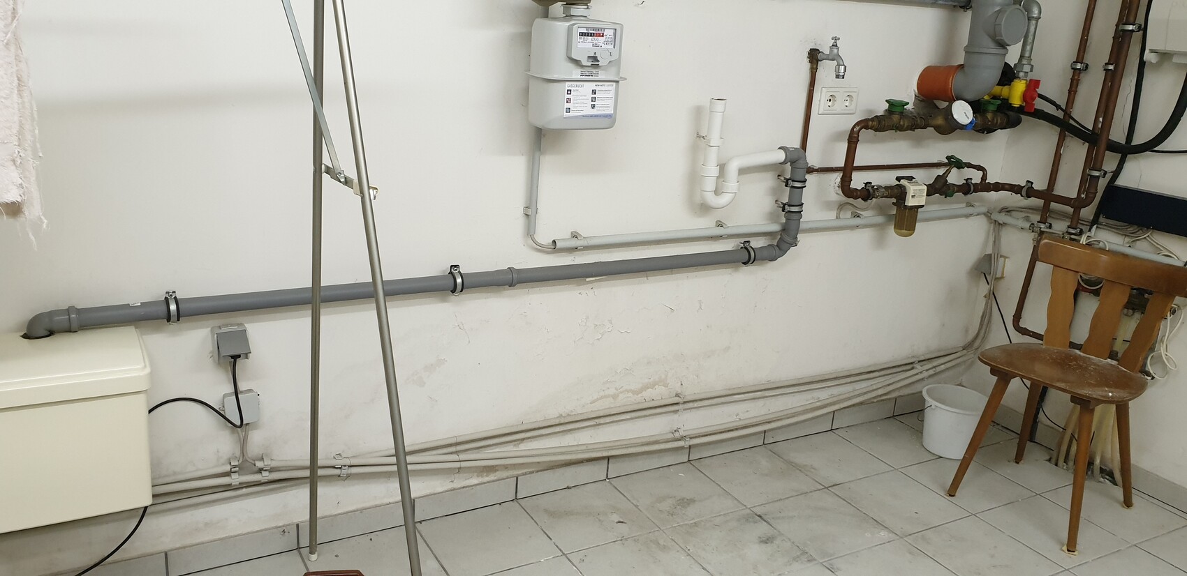 Kellerraum mit Gaszähler, Rohrleitungen, Ventilen, Stuhl und Eimer.