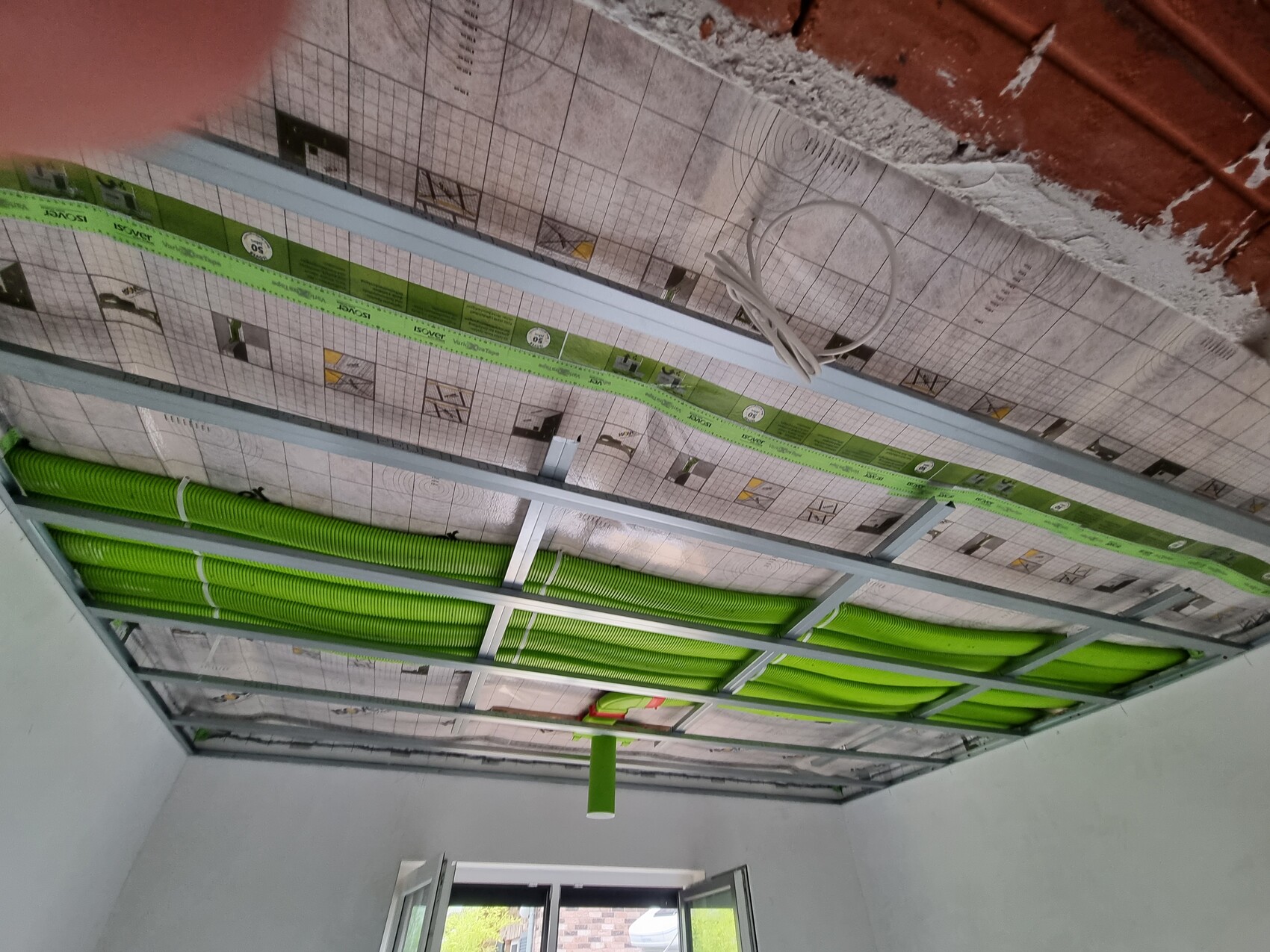 Decke mit grünen flexiblen Kabelrohren, Metallrahmen und Kabeln in Bauphase.