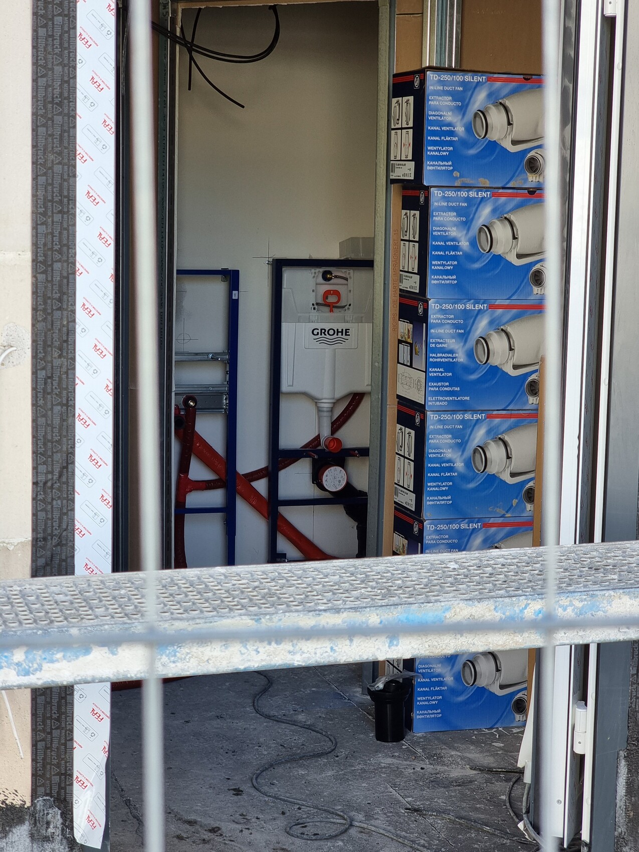 Blick in eine Installationskammer: Grohe-Spülkasten, rote Rohre, blaue Boxen, Geländer