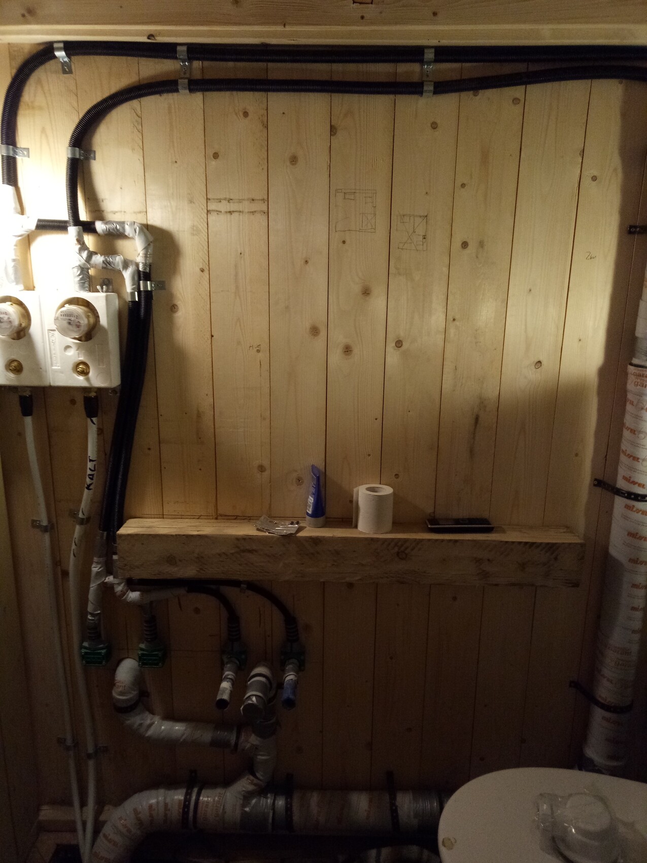 Haustechnikraum mit Rohren, Zählern und Holzwand im Keller.