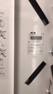 Bild zeigt Installationspanel mit Etikett und zwei schwarzen Montagehaltern an einer weißen Wand.