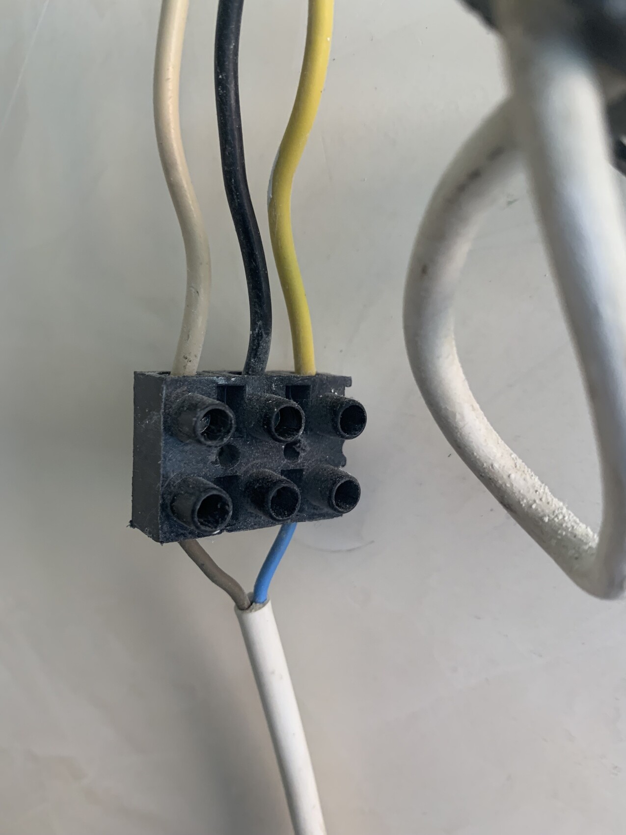 Klemmblock mit sechs Löchern; staubig, Leitungen weiß, schwarz, gelb, blau.