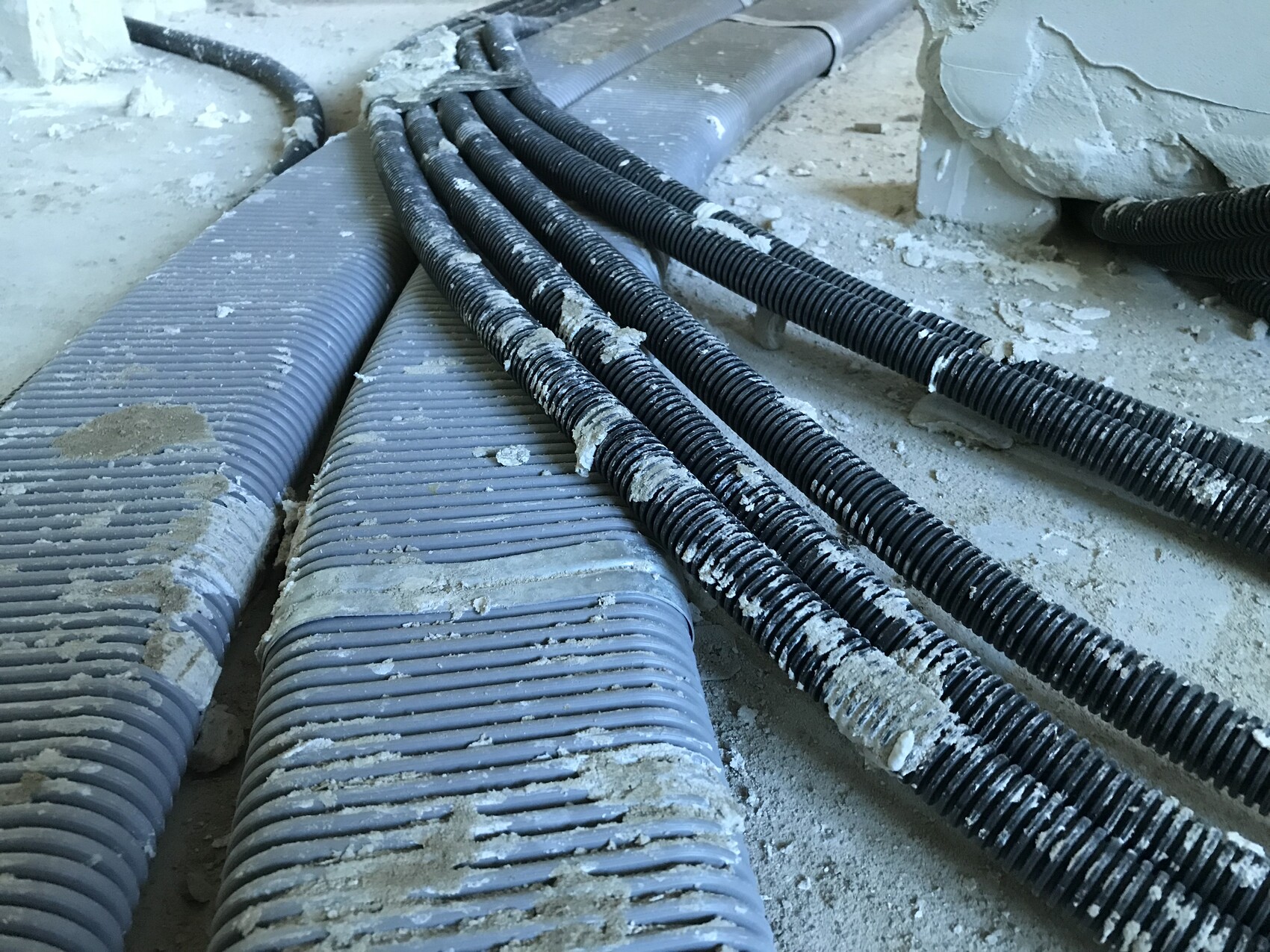 Baustelle mit schwarzen Kabelkanälen und Staub auf dem Boden