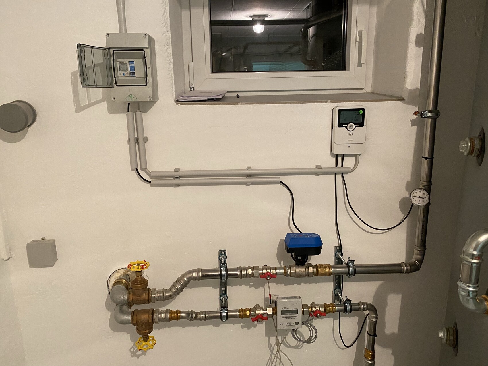 Sanitärinstallation: Metallrohre, Absperrventile, Druckmessgerät, Zählerkasten, Fenster dahinter