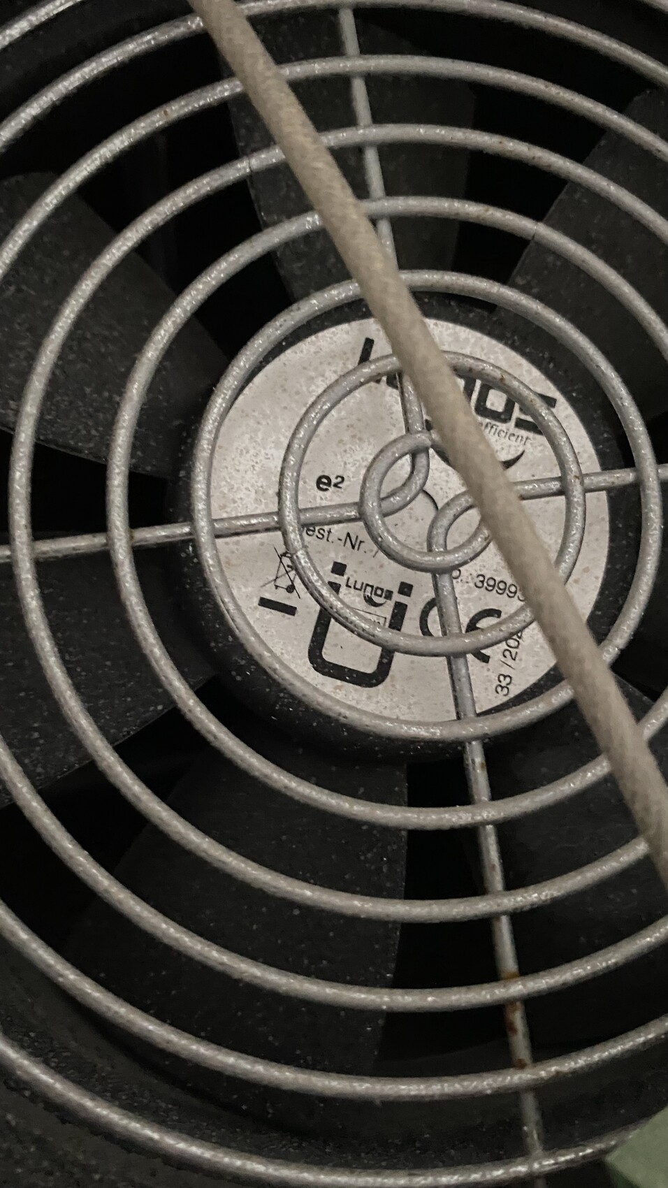 Nahaufnahme eines staubigen Ventilators mit Schutzgitter aus runden Metallringen.