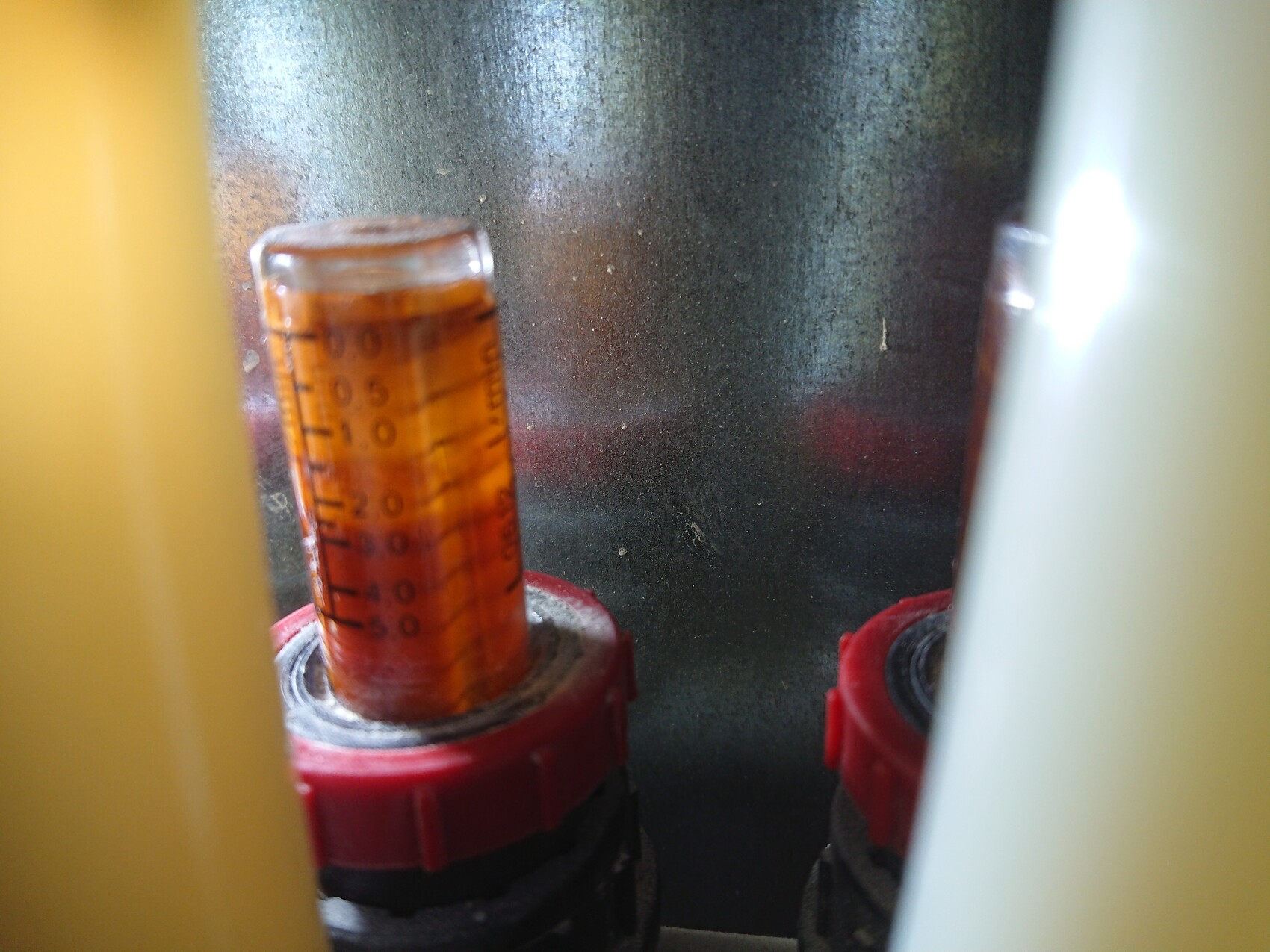 Nahaufnahme eines orangefarbenen Messröhrchens mit Skala, in rotem Halteclip.