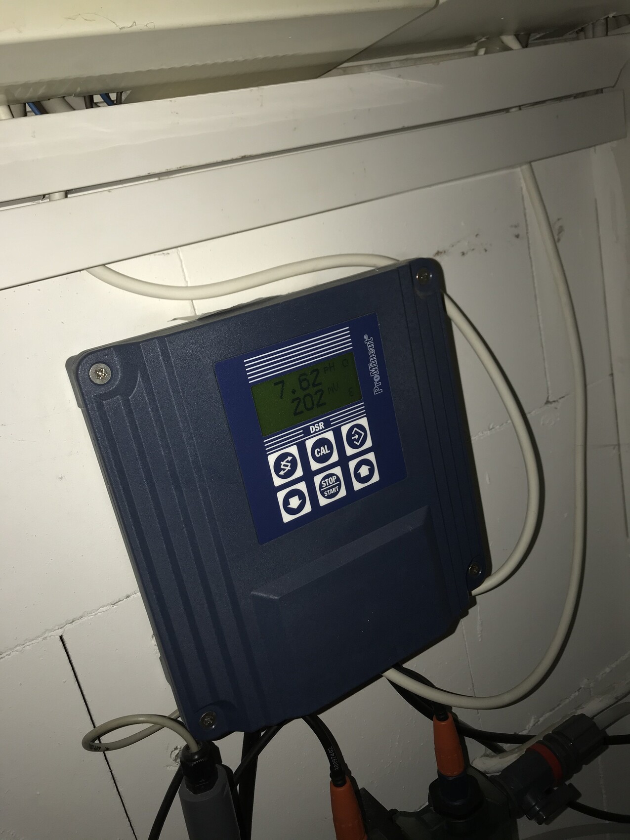 Blaues elektronisches Dosiergerät mit Display an der Wand, Kabel angeschlossen.