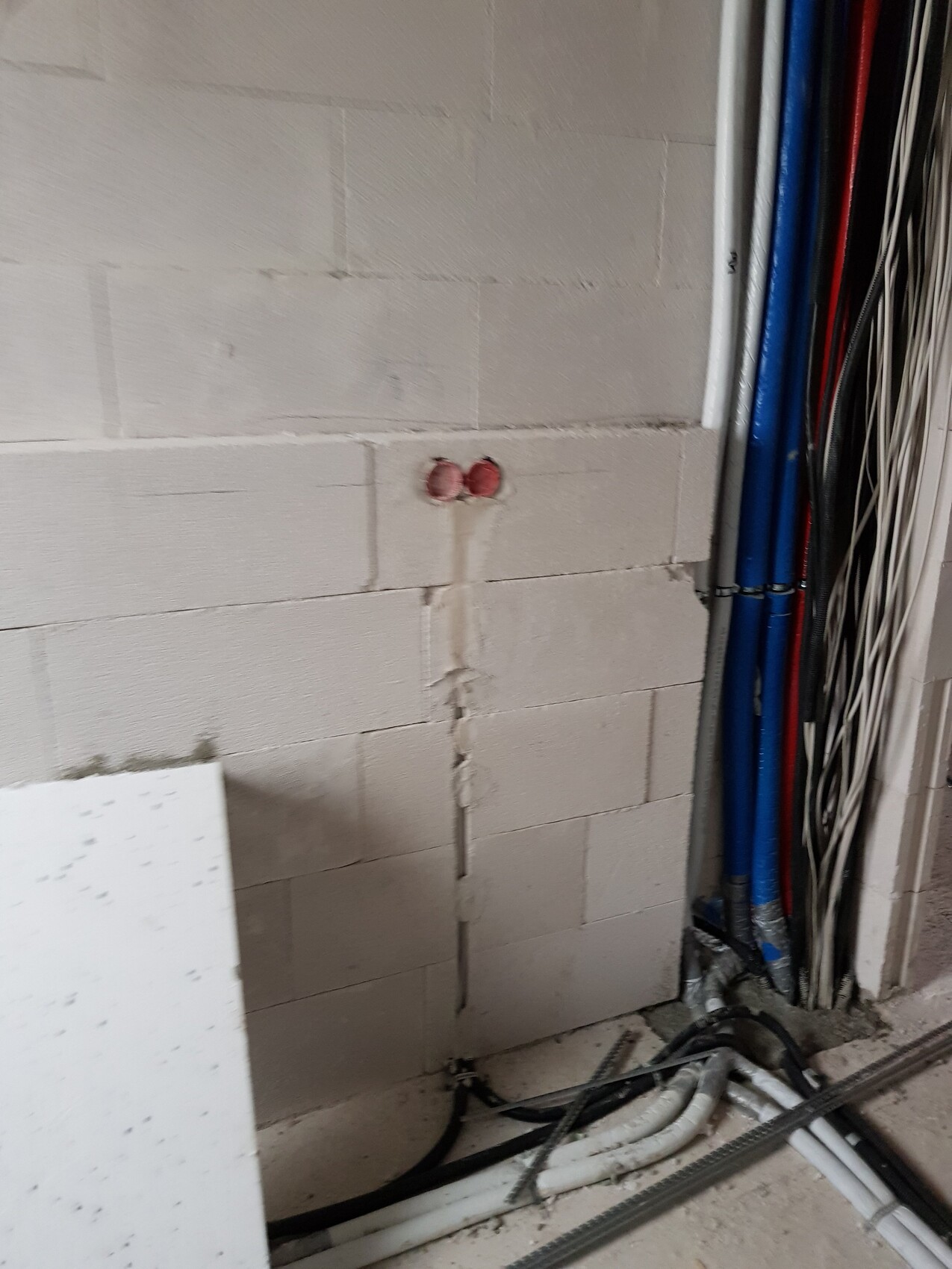 Kellerwand aus Porenbetonblöcken mit zwei roten Rohranschlüssen; daneben viele Kabel und Rohre.