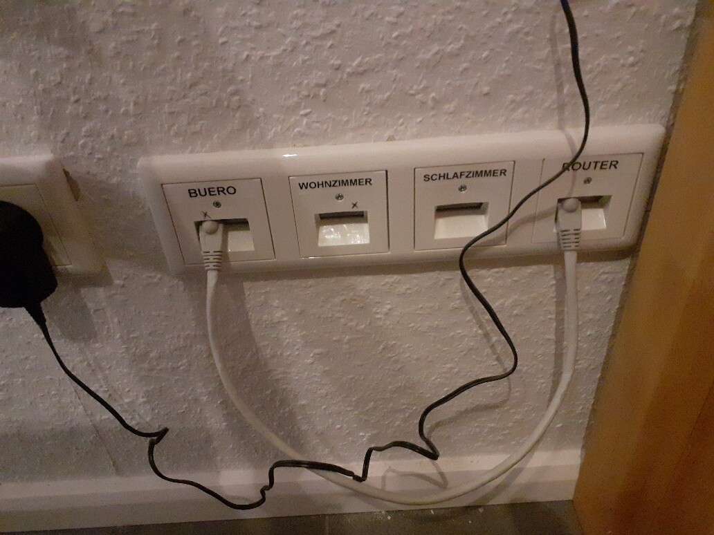Vier beschriftete Wandsteckdosen mit Kabeln; BUERO, WOHNZIMMER, SCHLAFZIMMER, ROUTER