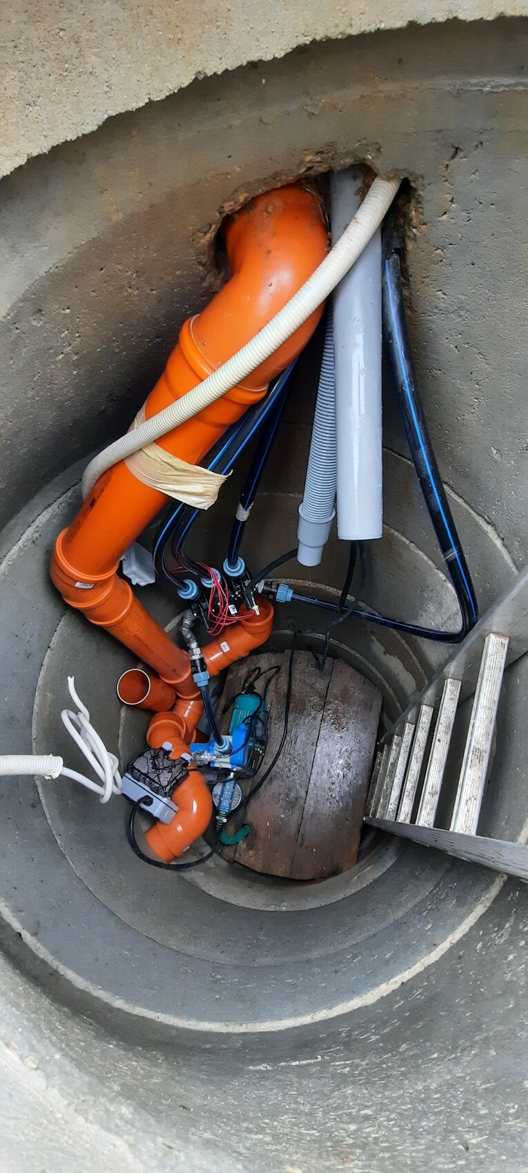 Unterirdischer Technikschacht mit orange Rohrleitungen, Kabeln und Werkzeug