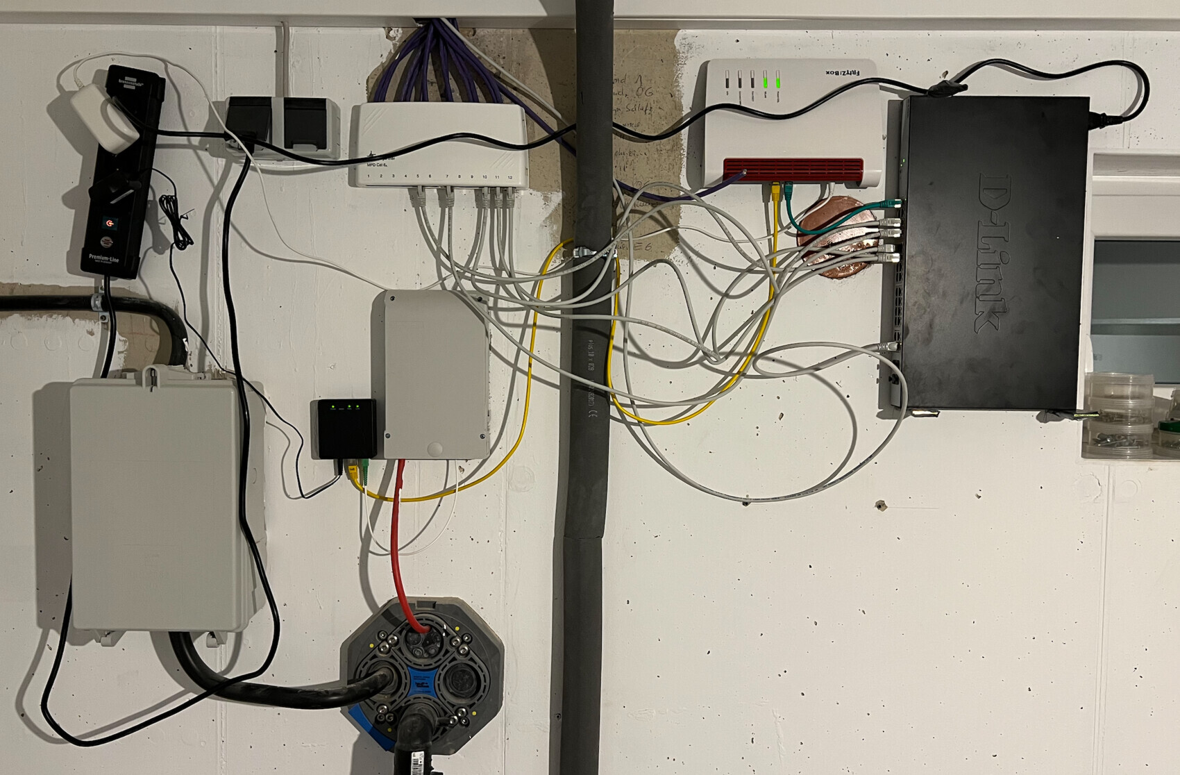 Wandmontierte Netzwerkinfrastruktur: D-Link-Gerät, Router/Switch, viele Ethernet- und Stromkabel.