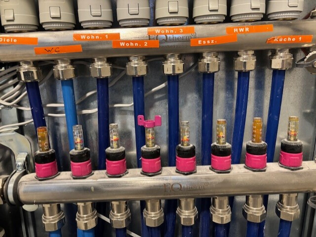 Verteilersystem: mehrere blaue Rohre mit pinken Ventilköpfen und orange Beschriftungsetiketten.