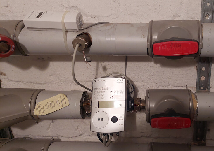 Keller-Heizungsrohrsystem mit Regler, Warmwasserzähler und roten Absperrventilen im Keller