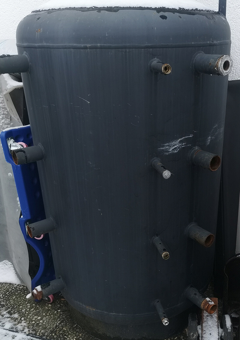 Großer dunkler Zylindertank mit mehreren Rohranschlüssen, außen im Schnee stehend.
