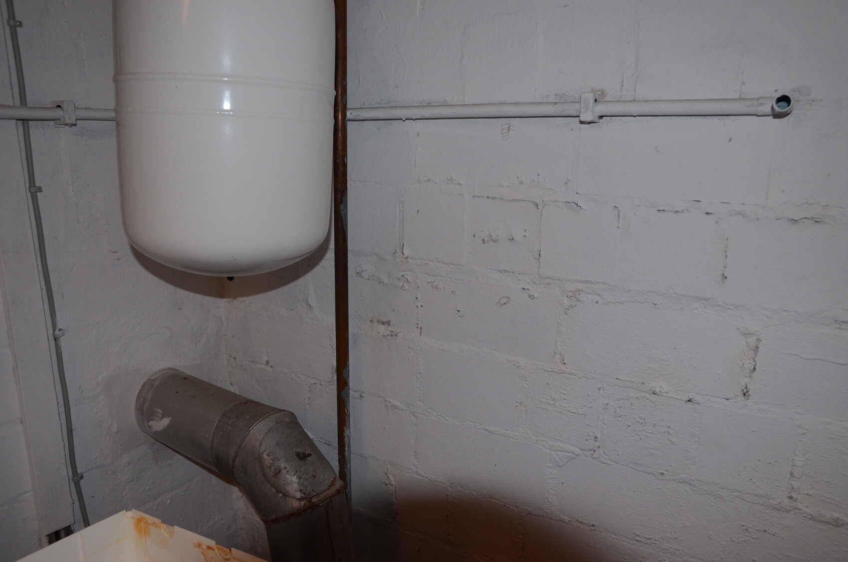 Weißer Druckausdehnungsbehälter an Kellerwand mit Rohrleitungen im Keller.