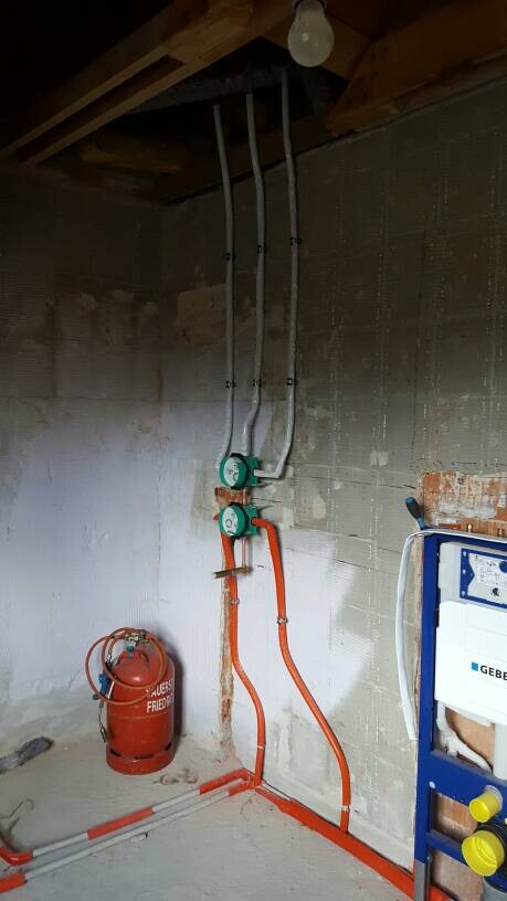 Kellerraum mit zwei Wasserzählern, orange Rohrleitungen und rote Gasflasche.