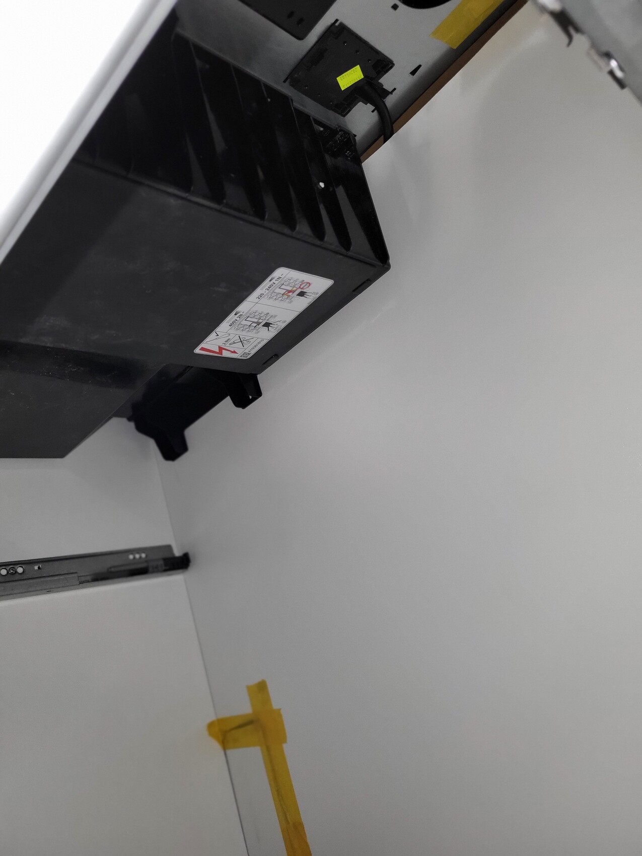 Schwarzes Elektronikgerät mit Lüftungsschlitzen, Warnetikett; Tür mit gelbem Klebeband.