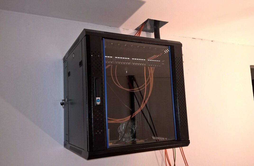 Verteilerschrank mit Kabelbündeln, Patchpanel und Netzwerkkabeln an der Wand.
