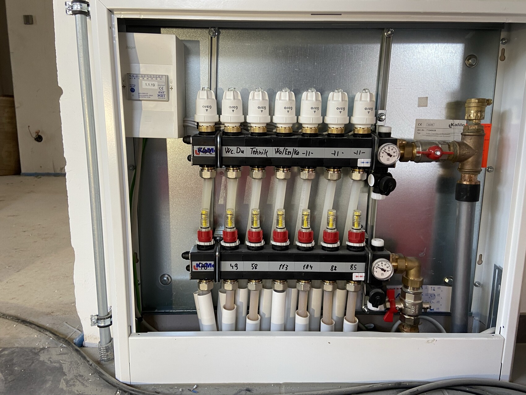 Eine Heizungs-Verteilerstation mit Ventilen, Thermostatköpfen und Druckmessgerät im Schrank.