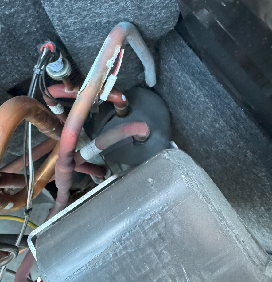 Mehrere kupferne Kühlleitungen mit Isolierung, verbunden mit einem schwarzen Filtertrockner.