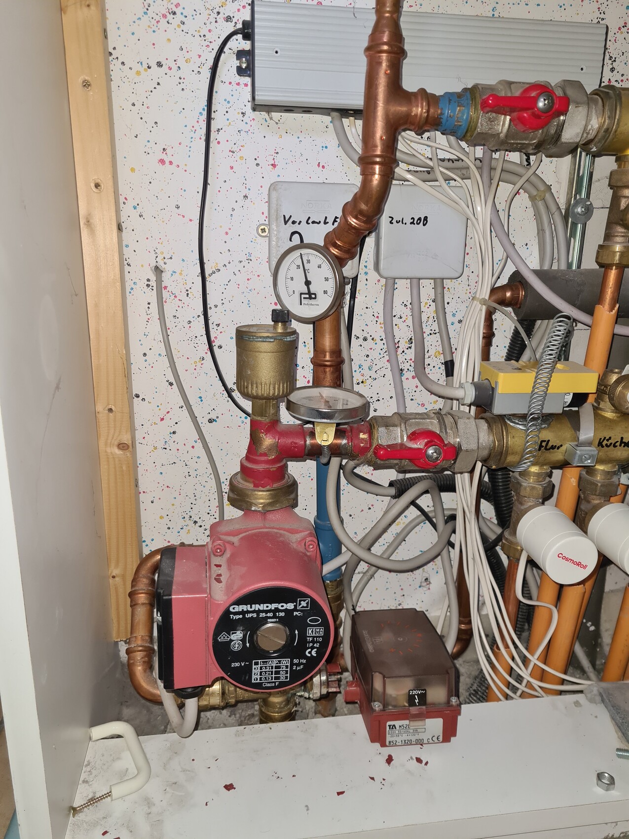 Rote Grundfos-Pumpe, Druckmesser, Kupferrohre, Ventile und Kabel im Heizungs-/Wassersystem.