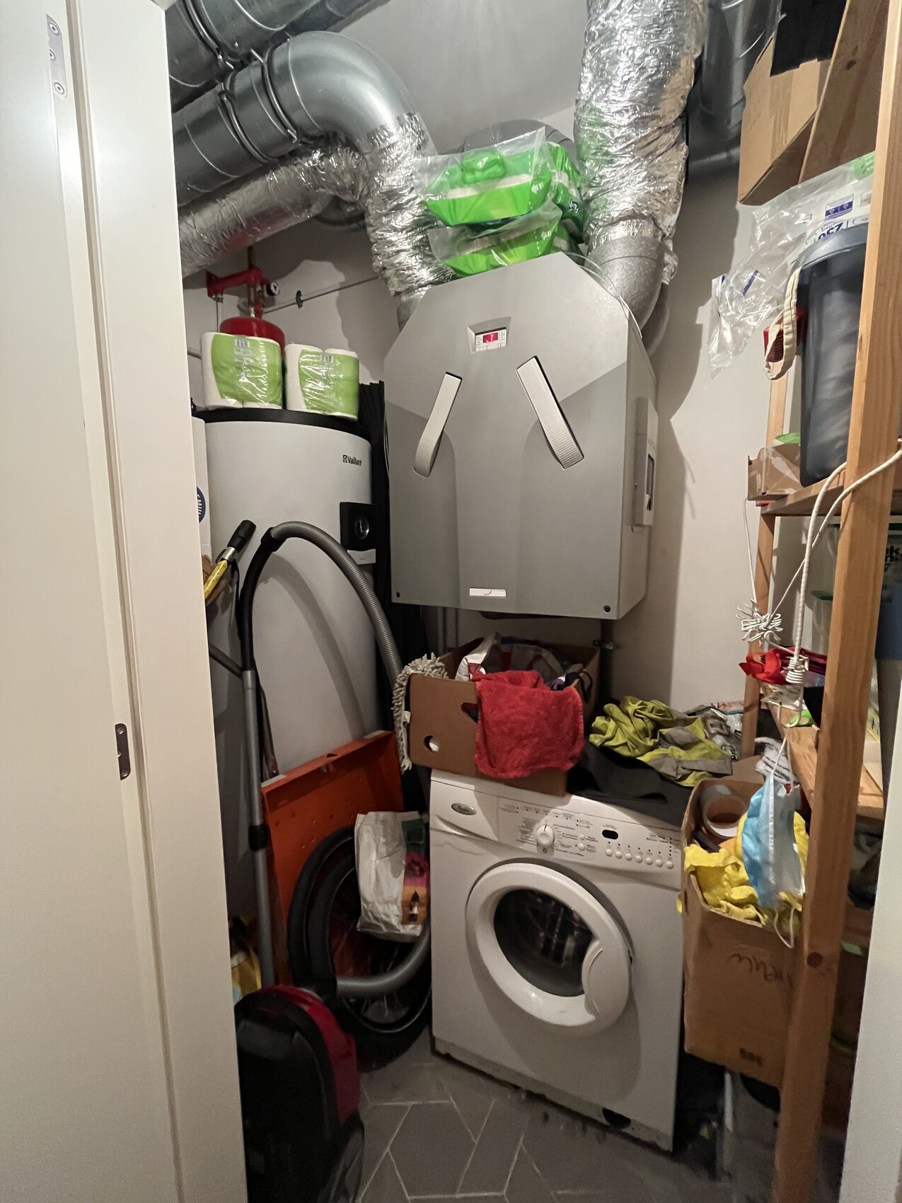Kleiner Abstellraum mit Waschmaschine unten und Wandheizgerät/Boiler darüber, viele Rohre.