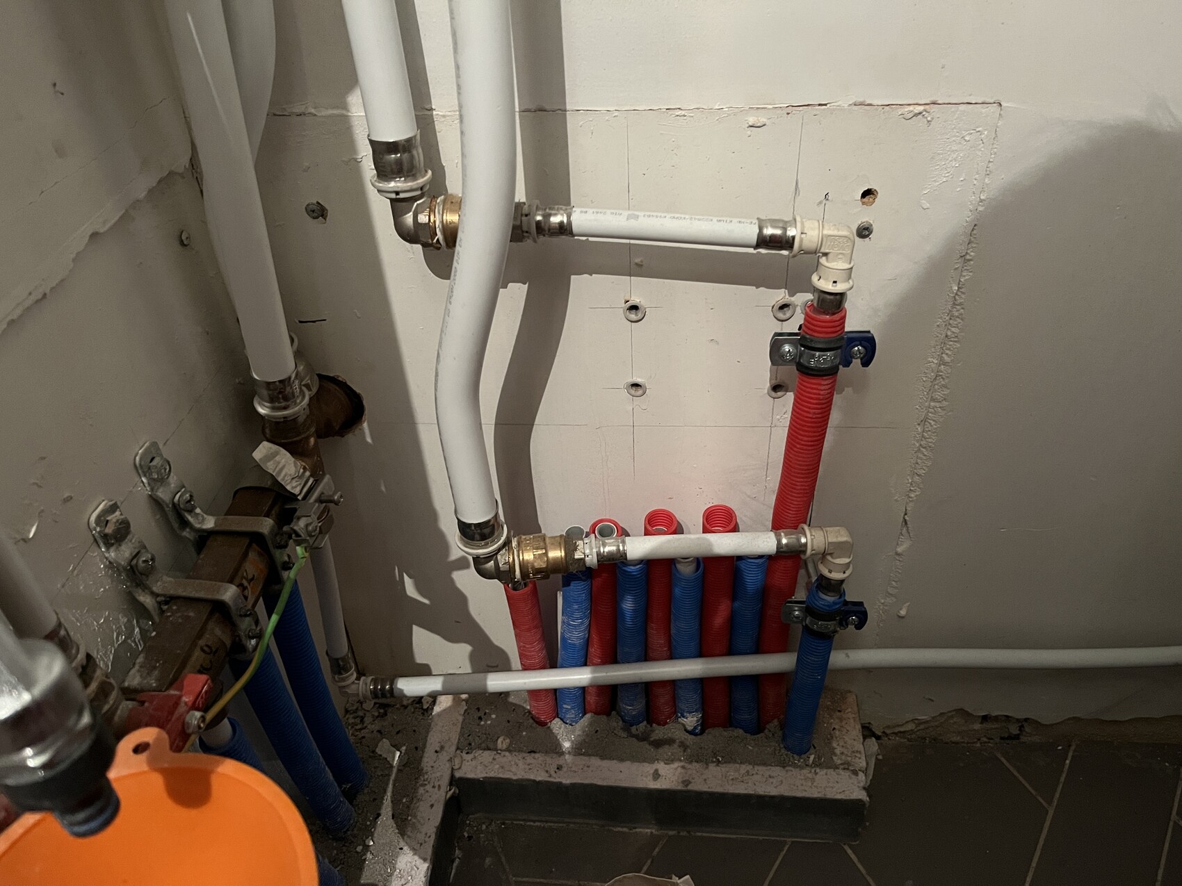 Installationsraum mit farbigen Wasserleitungen (rot heiß, blau kalt) und Ventilen.