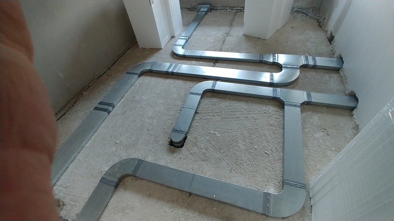 Metallische Haustechnik-Leitungen verlaufen über einen unbehandelten Rohboden in einem Bau-Innenraum
