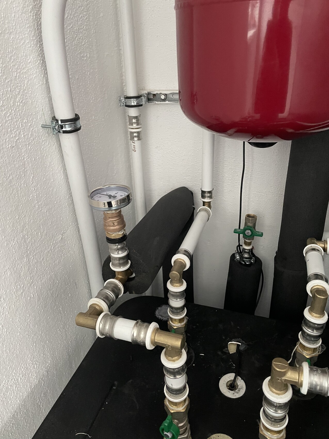Rohrleitungsanlage mit Druckmesser, Ventilen und rotem Ausdehnungsbehälter in Heizungsraum.