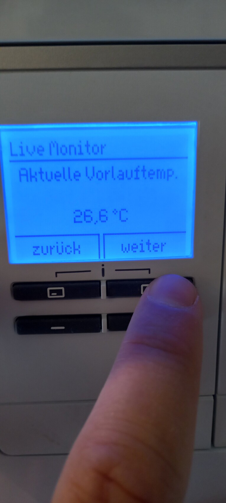 Heizungsregler mit blauem Display, Live Monitor; Vorlauftemp. 26,6°C; Finger am rechten Knopf.